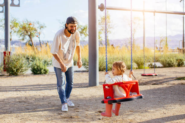 istock Father pushing daughter on swing in park 1282389500