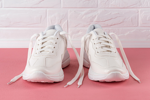 Pair of white chunky sole sneakers on a pink coral colored floor. New female or teen untied laces shoes for active lifestyle, fitness and sports. Front view.