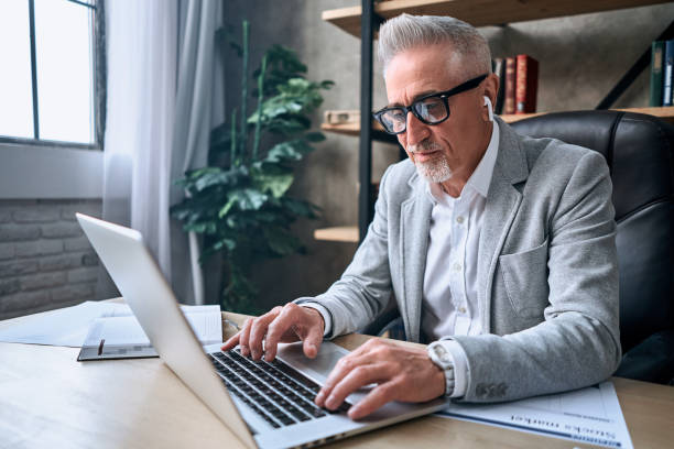 istock Stylish mature businessman looking at gadget screen at workplace 1282393387