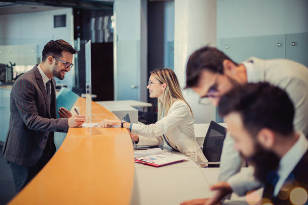 Sign here A young man is standing at a bank counter. Because of the good negotiation skills of an efficient employee, he decided to cooperate with her and sign a contract. bank teller stock pictures, royalty-free photos & images