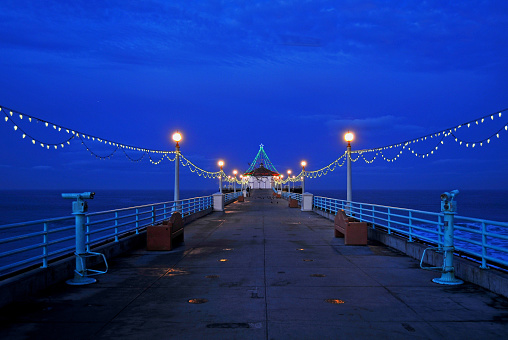 View from standing on the Manhattan Beach Pier facing west.  The pier decorated with Christmas lights illuminated with a dark, blue sky for a background.