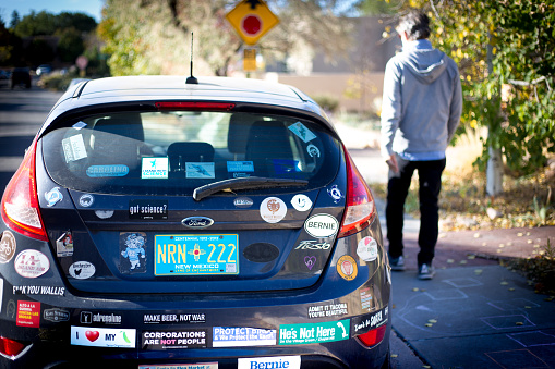 Santa Fe, NM: A pedestrian walks past a car plastered with bumper stickers in downtown Santa Fe, NM.