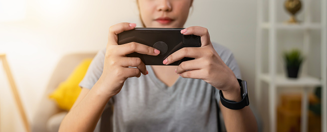 Young woman holding smartphone and play mobile games online on the table at the home.
