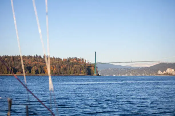 A view of Stanley Park and the Lion's Gate bridge from the bow of a sailboat motoring through. Taken in the fall, with the changing autumn leaves in Vancouver, British-Columbia.