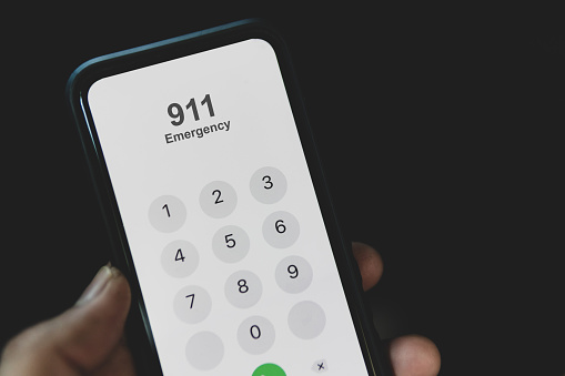 Hand holding cell phone with emergency number 911 on black background