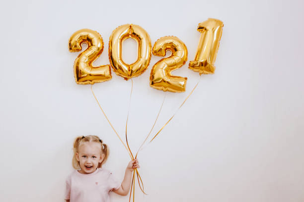 bambina che tiene palloncini d'oro con numeri d'oro 2021 su sfondo muro - 1 2 months foto e immagini stock
