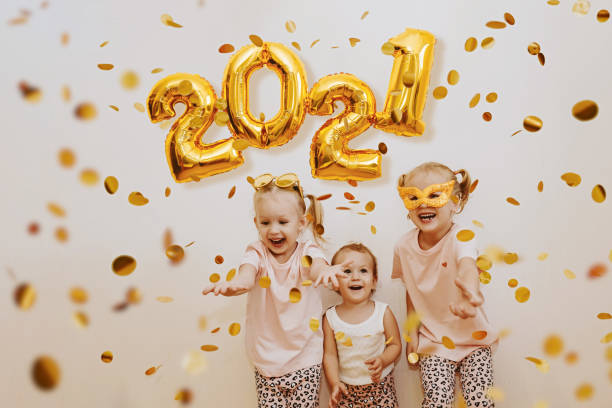 drei kleine mädchen genießen das fliegende goldene konfetti. feiern zu hause 2021 - 3 4 months stock-fotos und bilder