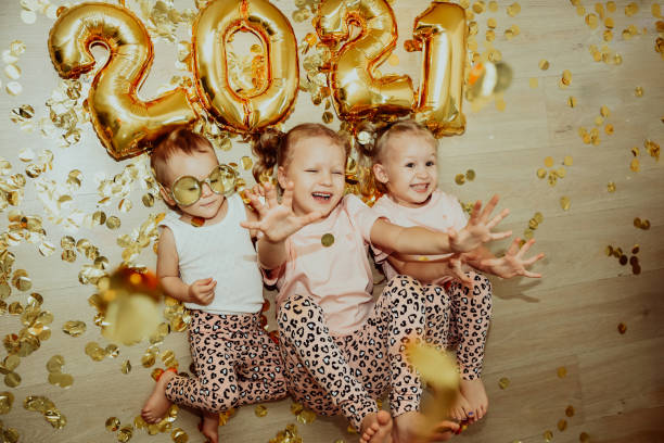 three little girls lying on the floor rejoice at the falling golden confetti. new year 2021 - child party group of people little girls imagens e fotografias de stock