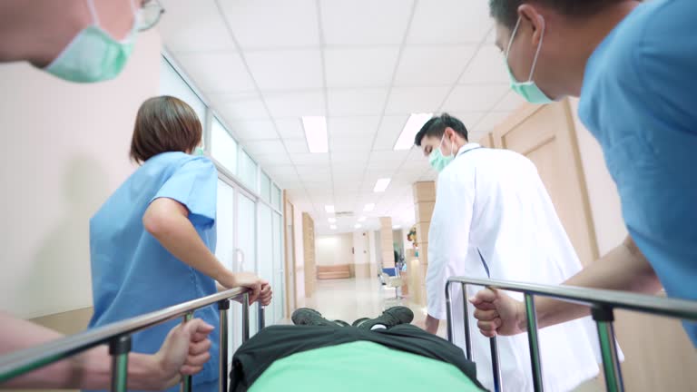 4K UHD Zoom out Point of view low angle shot: Patient on hospital gurney stretcher bed being transported down the hospital hallway by the medical team.