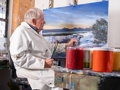 Mature male artist painting abstract art in his studio with squeegeeing.