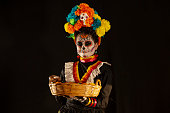 latin girl disguised as a skull for the day of the dead with an offering of candy, peanuts, oranges and snacks