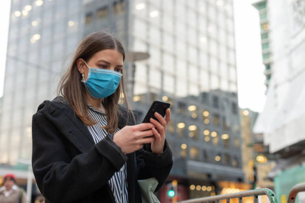 istock Young businesswoman with protective face mask using smartphone while commuting in downtown city street and city buildings with multi-coloured commercial signs at night 1282429057