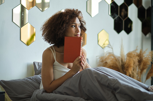 Young black woman reading on bed. beautiful lady resting at home.