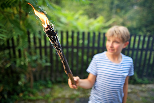 Little boy playing with burning stick taken from a bonfire. The boy is pretending to hold a torch.\nNikon D850