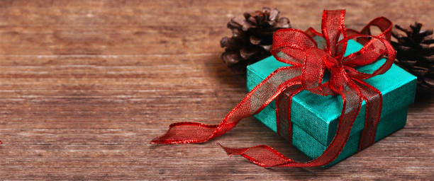 istock Top angle view green glitter gift box tied with red ribbon with pinecone on wood table 1282442306