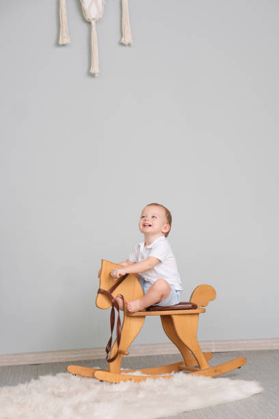 Child Sitting On Ride On Toy In Playroom. Toddler Baby Boy Riding Swinging On Rocking Chair Toy Horse