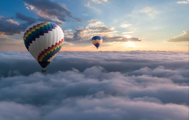 ballon à air chaud coloré volant au-dessus des nuages - blowing a balloon photos et images de collection