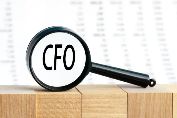 Closeup on businessman holding a card with text CFO, business concept image with soft focus background. Magnifying glass on the background of columns of numbers.