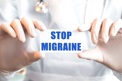 Doctor holding a card with text STOP MIGRAINE in both hands. Medical concept,