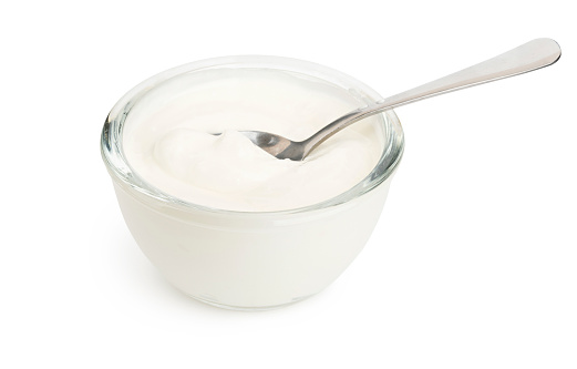 White yogurt in a glass bowl and spoon isolated with soft shadow