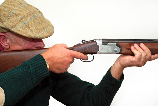 Double barreled twelve bore shotgun aiming and shooting, showing wooden carved stock, barrel and ornate gun illustrating the country outdoors sport of either clay shooting or rough shooting