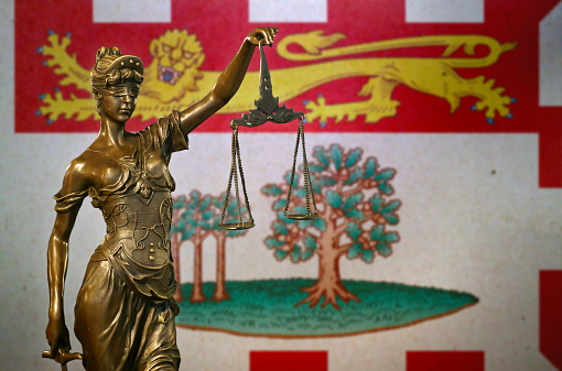 Close-up of a small bronze statuette of Lady Justice before a flag of Prince Edward Island (Canada).