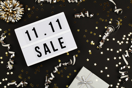 11.11 sale text on white lightbox, holiday ribbon and box on black background. Online shopping, singles day sale concept. Top view copy space
