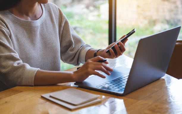 istock a woman holding and using mobile phone and laptop computer in office 1282453905