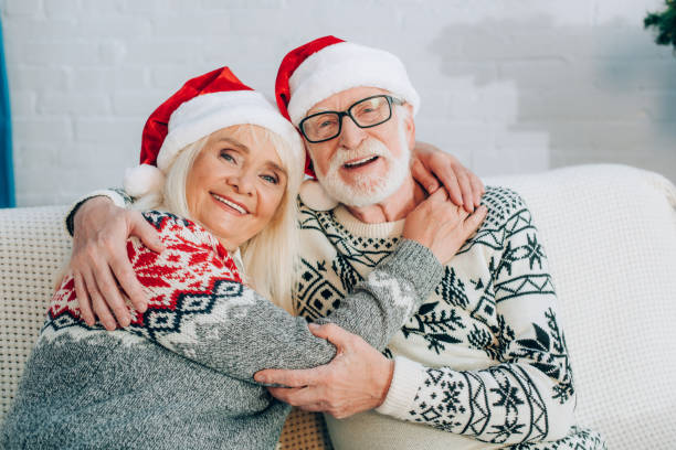 istock happy senior couple in santa hats embracing while looking at camera 1282456009