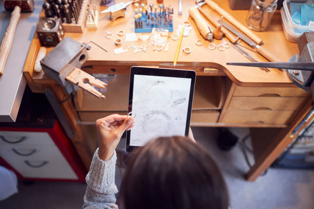 overhead view of female jeweller comparing ring with drawn design on digital tablet in studio - customized imagens e fotografias de stock