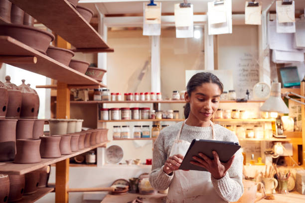 Female Potter In Ceramics Studio Checking Orders Using Digital Tablet Female Potter In Ceramics Studio Checking Orders Using Digital Tablet pottery making stock pictures, royalty-free photos & images