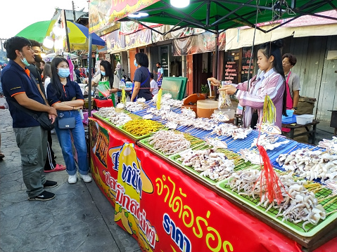 Kad Kong Ta, Lampang, Thailand.- Oct25, 2020 : People stand in front of grilled squid stall, with many kind of fresh squid placed on table at stall, at night market on october25, 2020.