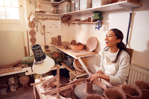Female Potter Shaping Clay For Pot On Pottery Wheel In Ceramics Studio