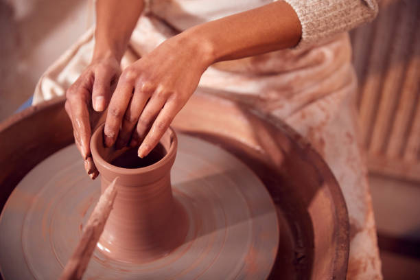 close up of female potter shaping clay for pot on pottery wheel in ceramics studio - throwing wheel photos et images de collection