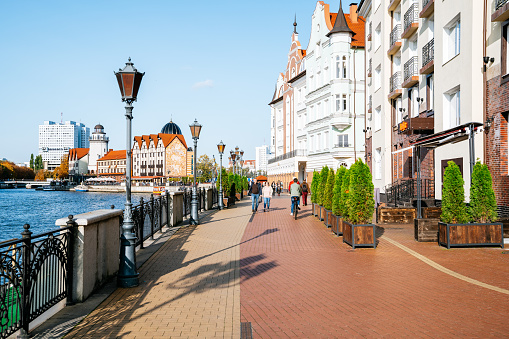 Kaliningrad city centre - People strolling along Fishing Village embankment. The Fishing Village, situated on the banks of the River Pregel between the Honey Bridge and High Bridge, recreates a slice of the city's pre-war fishing quarter with a series of cafes, restaurants and hotels housed within old German-style architecture and a 31-metre high lighthouse.
