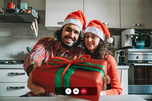 Screenshot of a Christmas video call. Millennial man and woman celebrating Christmas respecting social distancing. They are looking at camera. New normal during Coronavirus Covid-19 pandemic concept.