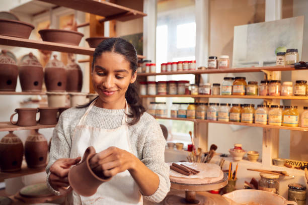 Female Potter Fitting Clay Handles To Mugs In Ceramics Studio