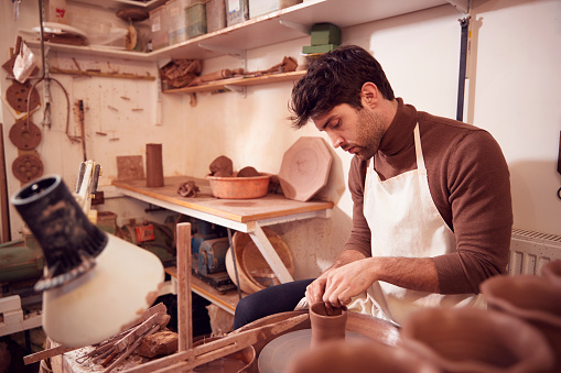 Male Potter Shaping Clay For Pot On Pottery Wheel In Ceramics Studio
