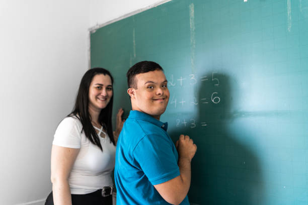 portret ucznia o specjalnych potrzebach piszącego na tablicy, nauczyciela u jego boku - education classroom advice mathematics zdjęcia i obrazy z banku zdjęć