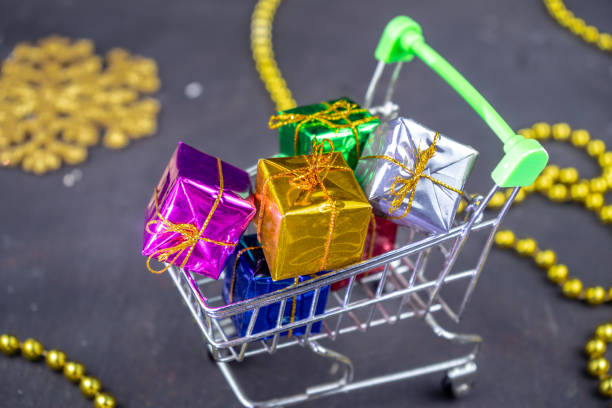 Shopping cart full of minimal present boxes. Gifts for Christmas or New Year with holiday decoration. Black background stock photo
