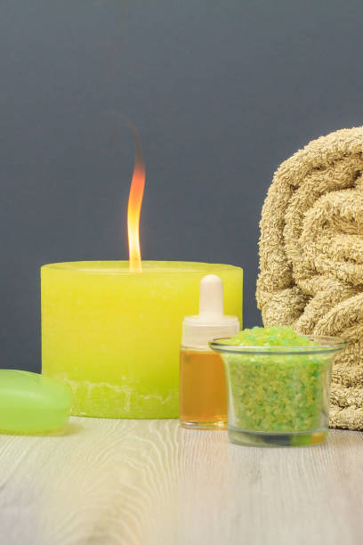 Spa composition with soft terry towel, bowl with sea salt, bottle of aromatic oil, soap and burning candle on gray background. Products for massage, facial and body care.
