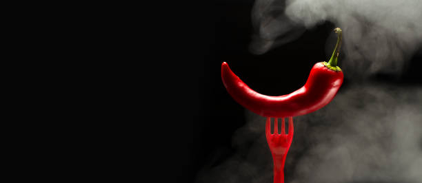 istock Hot red pepper on the red fork, steam against black background.Empty space 1282460895