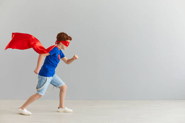 灰色の壁の背景に走るスーパーヒーローの衣装を着た小さな男の子。 - superhero child creativity little boys ストックフォトと画像