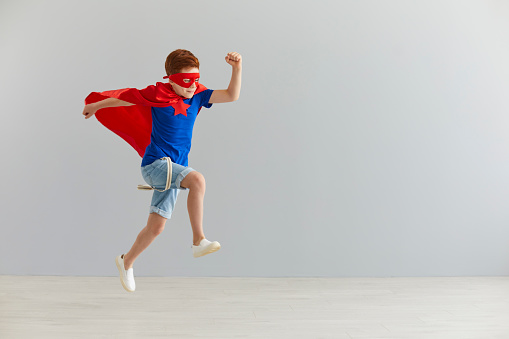 Happiness, freedom, childhood, movement and people concept, boy in red superhero cape and mask jump and fly.