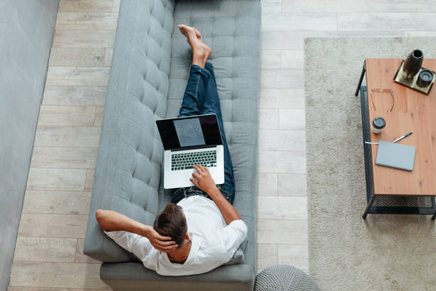 istock young man with a laptop lying on the couch 1282463903
