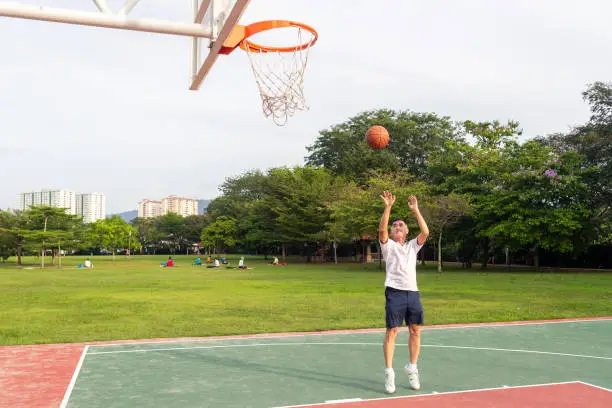 Senior sportsman throwing basketball in basket while practicing outdoors sports court