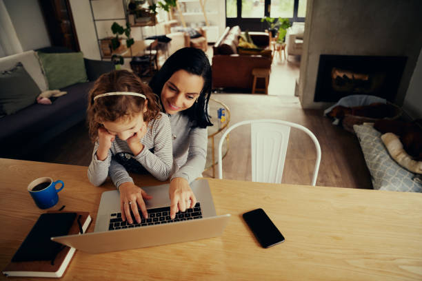 istock High angle view of smiling successful businesswoman working from home using laptop with daughter at home 1282467006