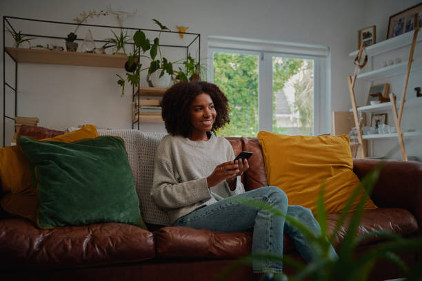 istock Positive woman using smartphone while sitting at home looking away 1282467653