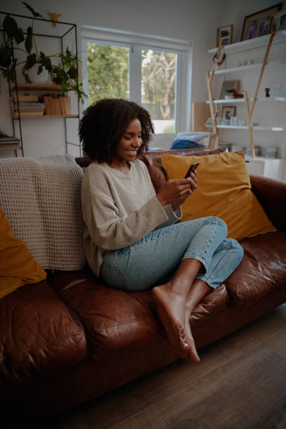 istock Beautiful african female watching video on smartphone at home while relaxing on couch 1282467760