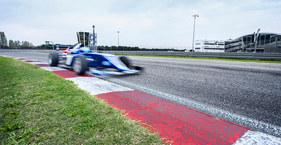 Blurred motion of blue open-wheel single-seater racing car car driving on track.